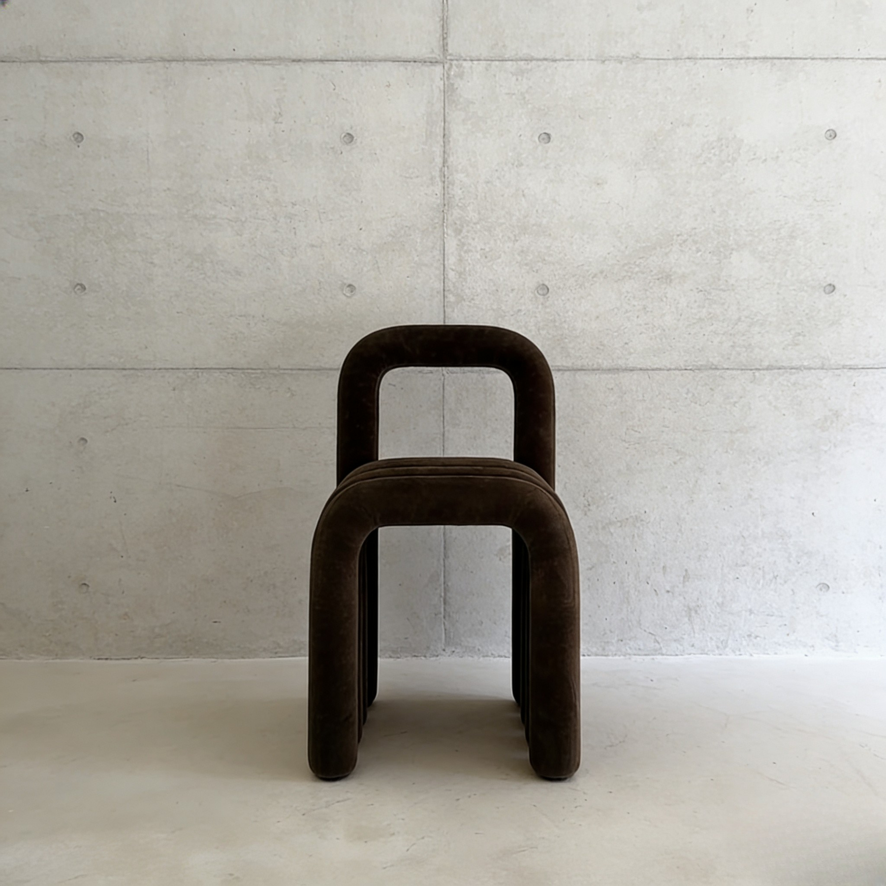 A brown stool curved against a concrete wall.