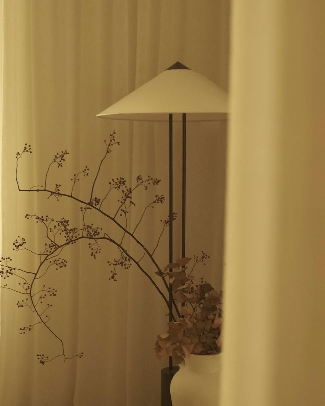 Decorative floor lamp with a vase of branches against a beige curtain