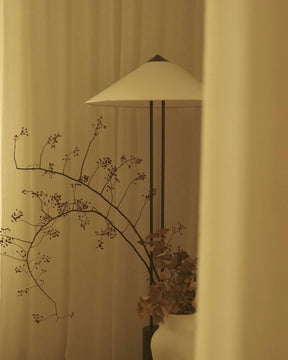 Decorative floor lamp with a vase of branches against a beige curtain
